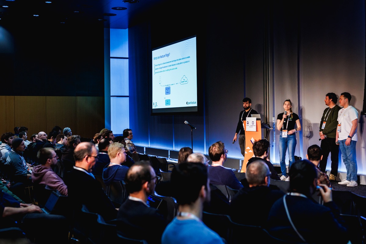 Four speakers on stage at KubeCon EU 2026 in front of a full room, with a "What are feature flags?" slide projected behind them